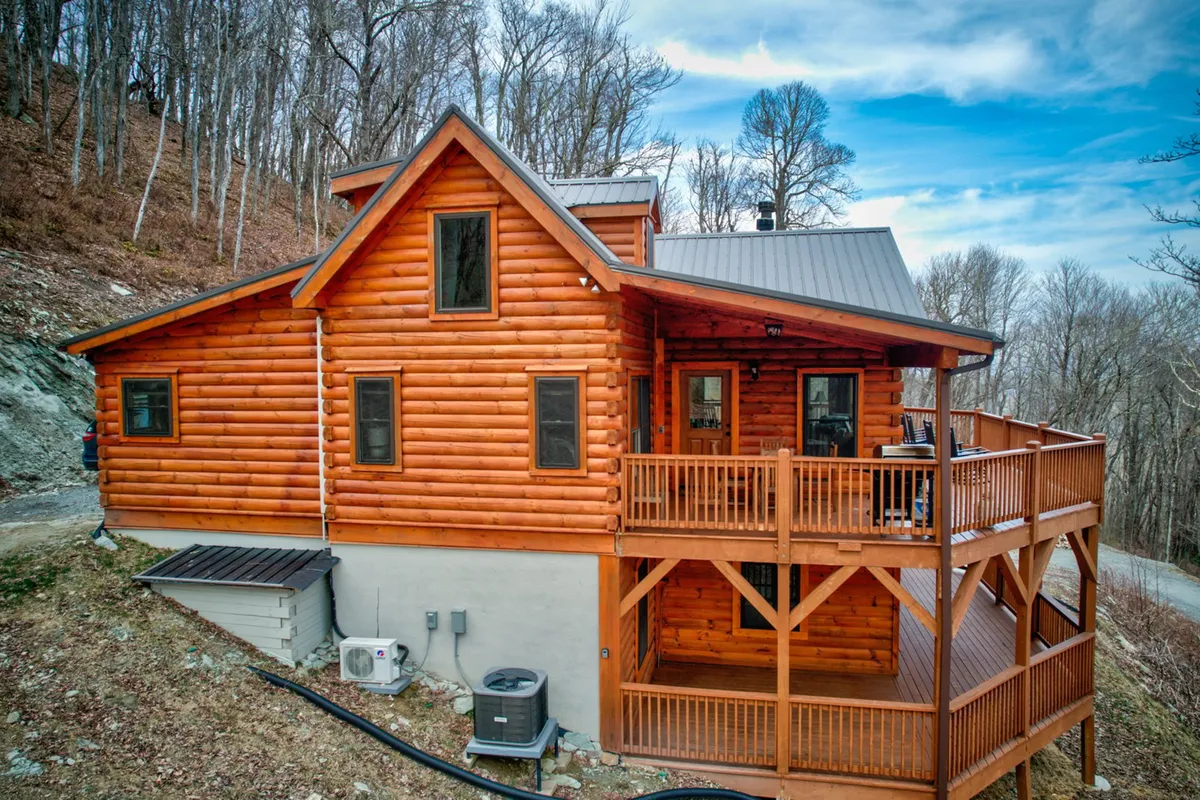 The log cabin’s wooden deck, nestled among mature trees, offers a warm and welcoming space for outdoor relaxation and gatherings. The image communicates a sense of peace and togetherness in nature, with the deck serving as an ideal spot for socializing or quiet reflection.
