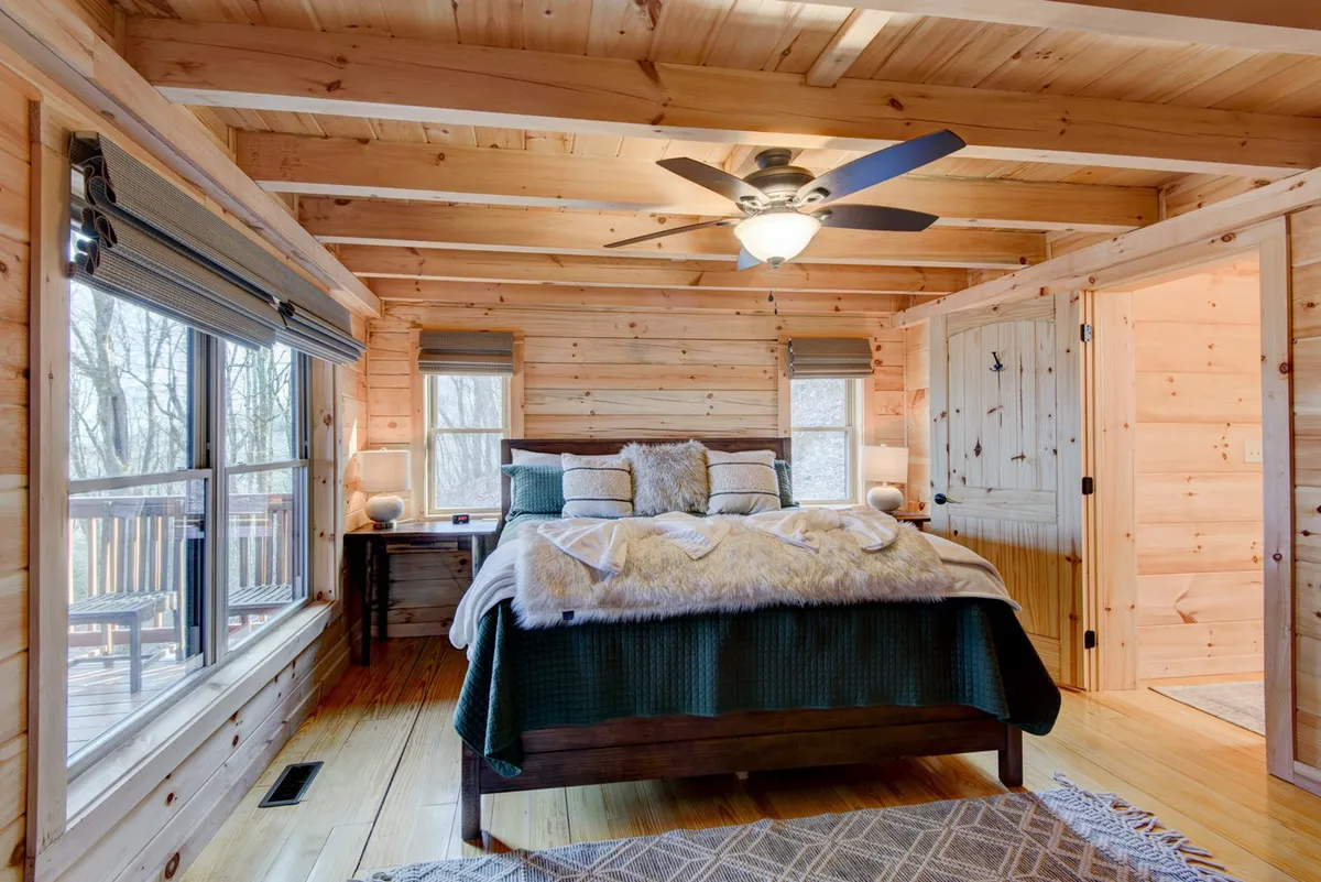 A serene bedroom with plush bedding, large windows that invite in natural light, and wooden walls that create a cozy, rustic atmosphere. The bed is positioned to capture the beautiful views outside, offering a peaceful setting for relaxation.