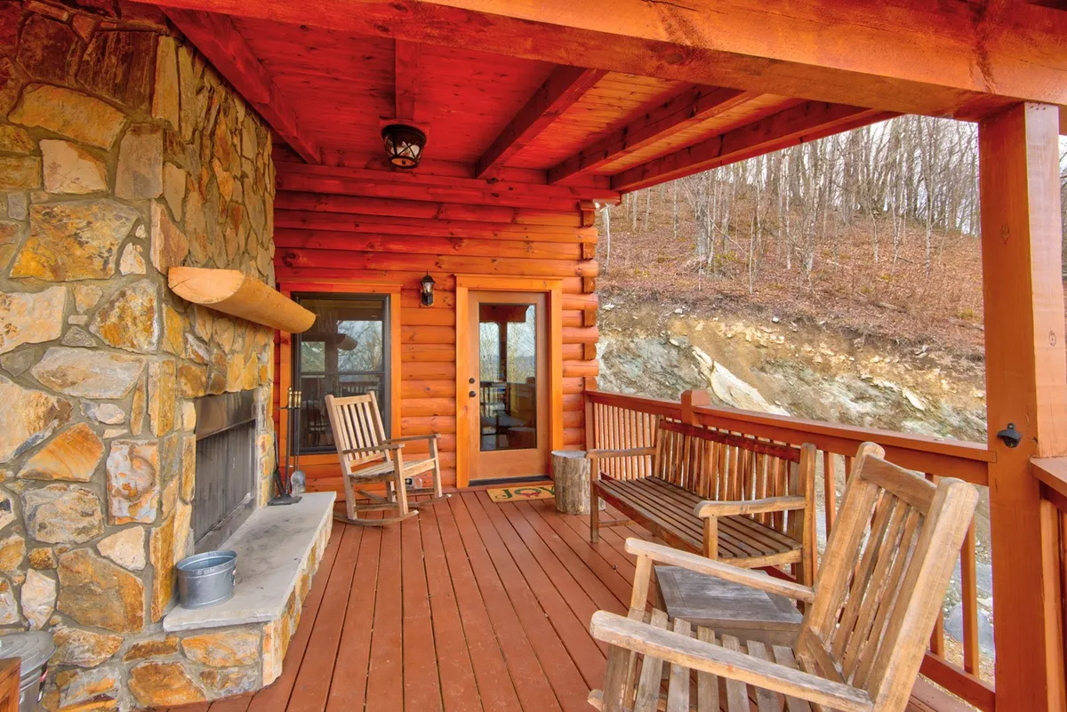 This exterior shot highlights a rustic porch with log walls, a stone fireplace, and wooden rocking chairs—an inviting spot for relaxing, entertaining, or observing wildlife throughout the year. The setting merges outdoor living with cozy, communal ambiance.