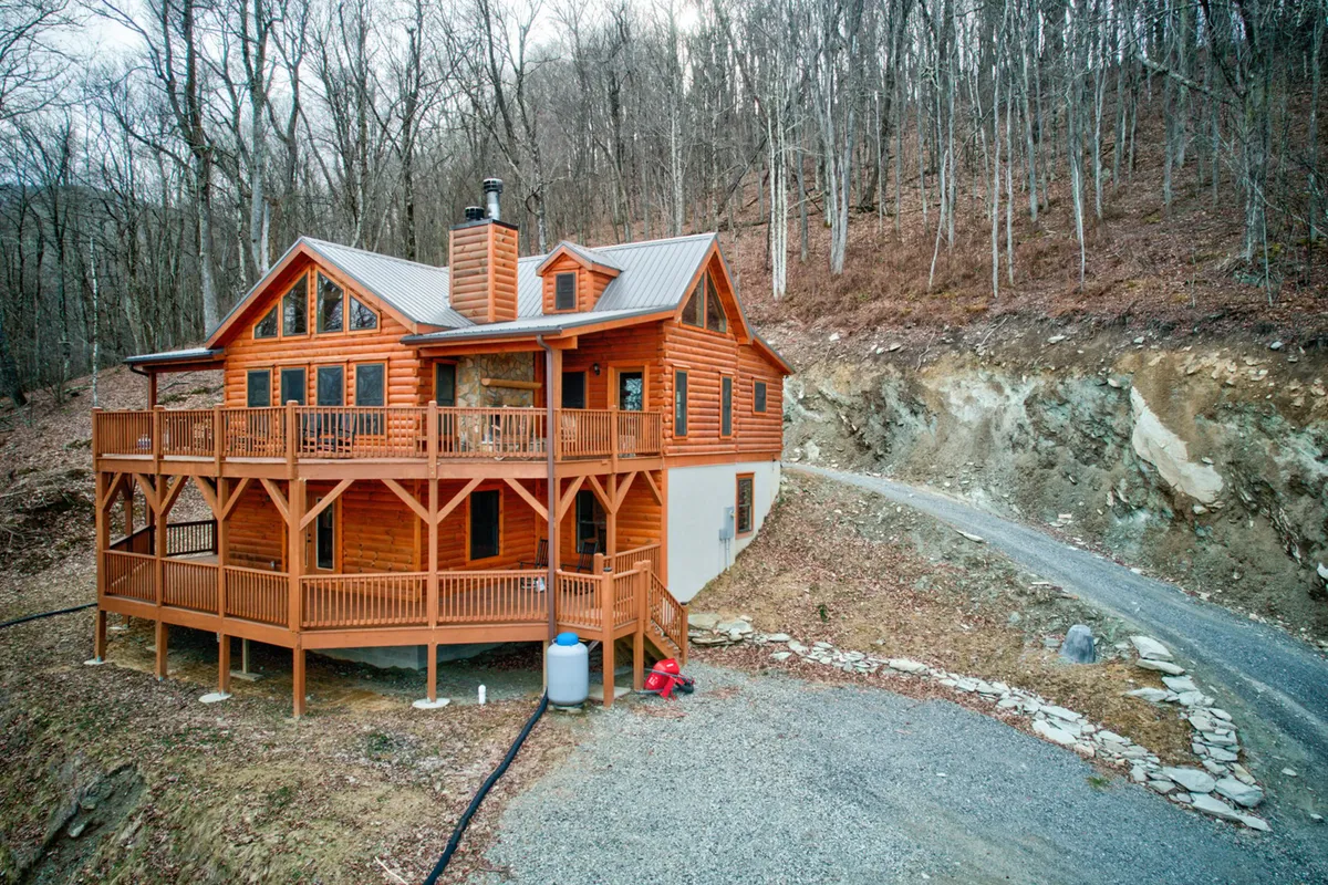 A wide shot of the log cabin with its large deck, surrounded by trees and a gravel driveway. The setup suggests both seclusion and easy access, reinforcing the blend of privacy and proximity to activities described in the section.