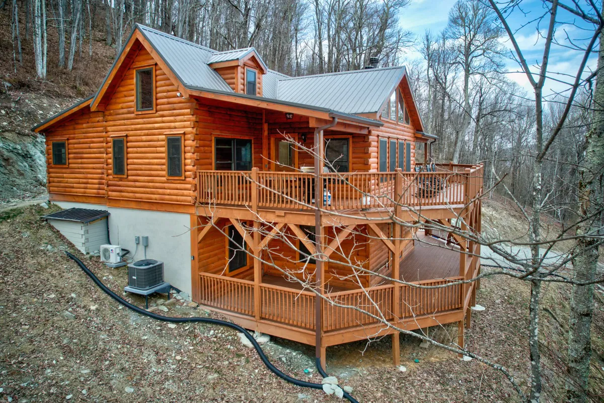 This image showcases the exterior of High Time Cabin, highlighting its classic log cabin structure, a spacious deck, and the lush surrounding trees. The sunset light adds a cozy and welcoming atmosphere, inviting visitors to picture themselves arriving at this mountain retreat.