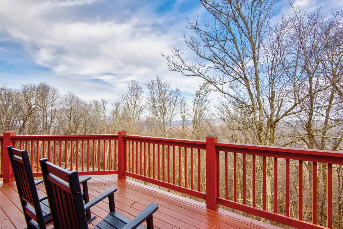 This image showcases a peaceful wooden deck with rocking chairs facing out toward distant trees and an open sky. The setting is tranquil, inviting guests to sit and enjoy nature across seasons. The view suggests the changing beauty of the landscape, from lush greenery in summer to frosted trees in winter.