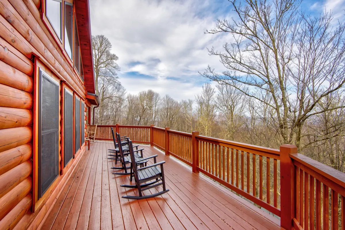 A serene exterior view highlighting wooden rocking chairs lined up along a deck with a sturdy railing, overlooking a lush natural landscape. The setting suggests peaceful moments spent watching wildlife or star gazing, with plenty of safe, open space for dogs to enjoy alongside their owners.